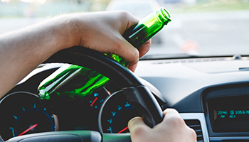 A person grips a beer bottle while driving a car