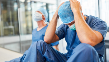 Two surgeons seated on the floor, hands on their heads